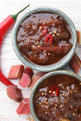 Tasty rhubarb sauce and ingredients on white wooden table, flat lay