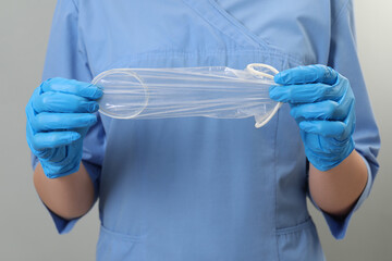 Doctor with unrolled female condom on light grey background, closeup. Safe sex