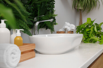 Fototapeta na wymiar Green artificial plants, vessel sink and different personal care products in bathroom