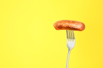 Fork with tasty fried sausage on yellow background. Space for text