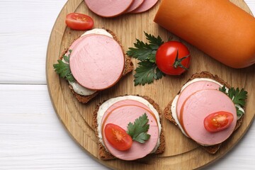 Delicious sandwiches with boiled sausage, tomato and sauce on white wooden table, top view