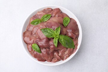 Bowl with raw chicken liver and basil on white table, top view