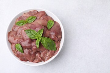 Bowl with raw chicken liver and basil on white table, top view. Space for text