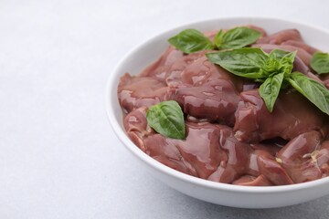 Bowl with raw chicken liver and basil on white table, closeup. Space for text