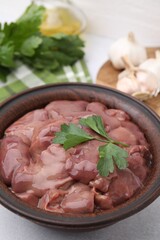 Bowl with raw chicken liver and parsley on white table, closeup