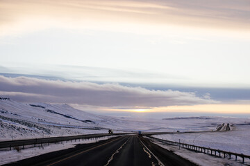 Beautiful winter landscape with a highway between blue snowy mountains, fluffy clouds on a sunset...