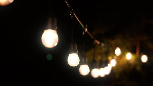 Outdoor string lights hanging on a line on outside house in backyard. Garden decoration. Party camping