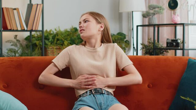 Sick ill woman suffering from painful stomach ache, period cramps lying on sofa at home room. Girl holding belly, feeling abdominal or menstrual pain. Abdominal pain, gastritis, diarrhea, indigestion