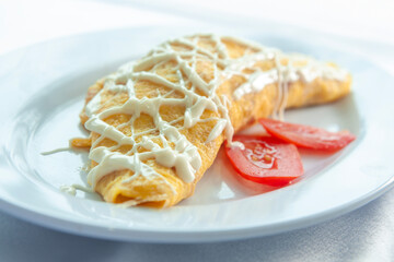 Rolled egg omelets filled with chicken garnished with mayonnaise and sliced ​​tomatoes are placed on a white plate