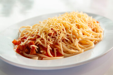 spaghetti bolognese with cheese sprinkled is placed on a white plate with a white background