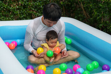Fototapeta na wymiar father and infant baby girl playing water with colorful plastic balls in inflatable pool