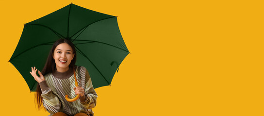 Beautiful young Asian woman with umbrella on yellow background with space for text - obrazy, fototapety, plakaty