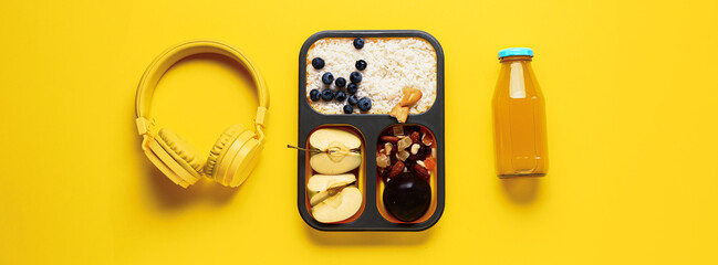 Bottle of juice, headphones and lunchbox with tasty food on yellow background