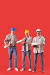 Team of male builders with paper rolls on red background