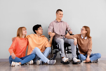 Fototapeta premium Group of teenagers with boy in wheelchair near light wall
