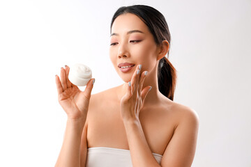 Beautiful Asian woman with cosmetic cream on white background