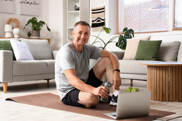 Sporty mature man with bottle of water and laptop at home