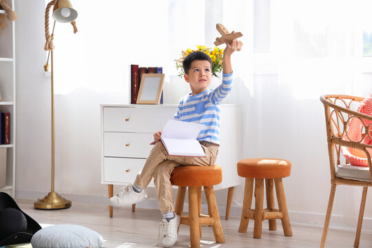 Cute little boy with adventure book and wooden airplane at home