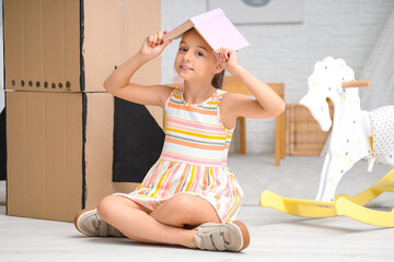 Cute little girl with adventure book and cardboard rocket at home