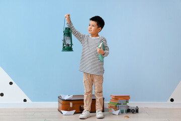 Cute little boy with adventure book and lantern near blue wall