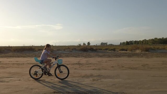 Little girl riding a bicycle on a sandy road as the sun shines at dusk, Catalonia, Spain