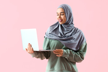 Young Muslim woman with laptop on pink background