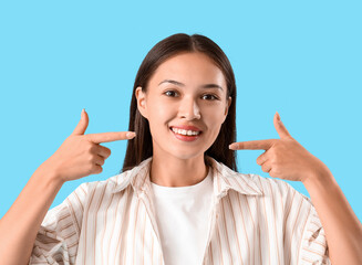 Young Asian woman pointing at her smile on blue background, closeup