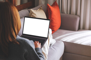 Mockup image of a woman working and typing on laptop computer with blank screen while lying on sofa at home