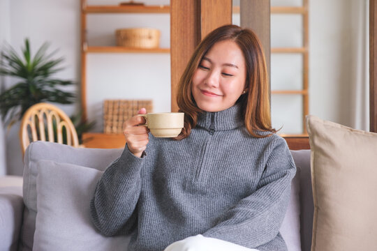 Portrait image of a beautiful woman holding and drinking hot coffee at home