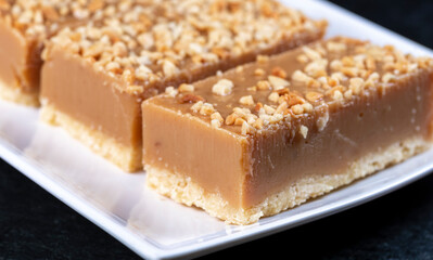 A piece of caramel slice covered with nuts on a white plate