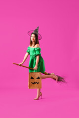 Young woman dressed for Halloween as witch with broom and gift bag on purple background