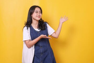 Young student woman presenting something to the side on yellow background