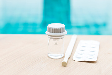Swimming pool water in glass vials with tablet reagents and stirring rod on swimming pool edge,...