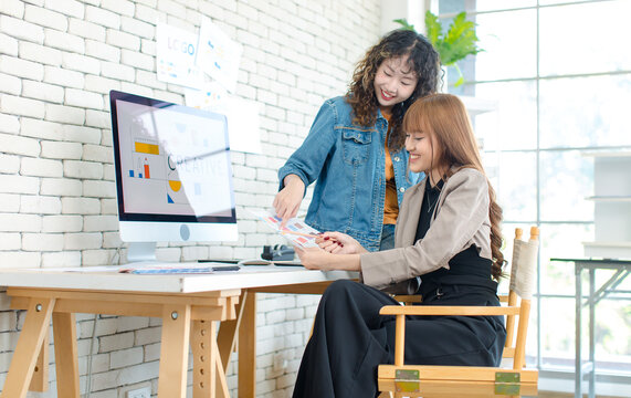 Asian professional successful young female creative graphic designer in casual outfit sitting smiling drawing sketching artwork with pencil when colleague helping thinking ideas in office workstation