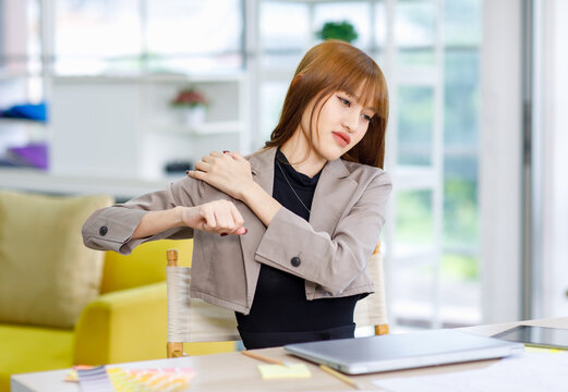 Asian professional successful overworked exhausted tired young female businesswoman creative graphic designer employee in casual suit blazer outfit sitting taking break stretching arms and shoulder