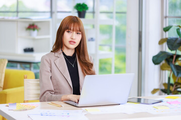 Asian professional successful young female businesswoman creative graphic designer employee in casual fashionable suit blazer outfit sitting working using typing laptop computer at office workstation