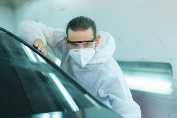 Professional automotive painting technician in chemical protecting suit inspecting car painting...