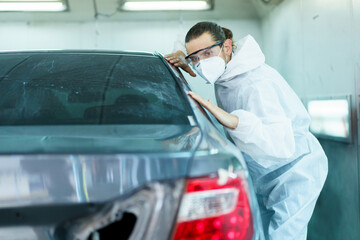 Professional automotive painting technician in chemical protecting suit inspecting car painting quality in painting chamber together. Car painting and detailing technicians portrait.