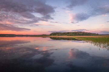Beautiful panoramic view of sunset on lake Snudy, Braslav kakes, Belarus. The sky is reflected on the surface of the lake red and dark blue colors. A dark forest is visible in the distance. 
