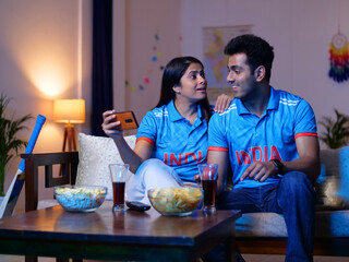 A young Indian man and a woman watching a live match on a mobile - T series  . Couple wearing...