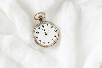 Vintage pocket watch showing New Year eve, holiday midnight on clock face, twelve hour, Antique watch on white fur background, empty space. New Year, Christmas, xmas concept, minimal composition