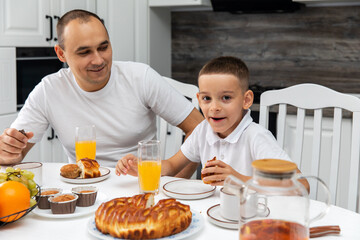 Portrait of a little boy and his dad sitting at the table during breakfast at home in the kitchen. The boy communicates with his dad during breakfast in the kitchen.