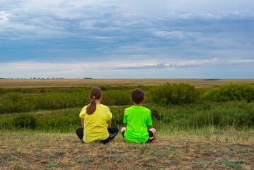 Fototapeta na wymiar Two children sitting in the steppe with their backs. High quality photo