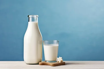 Foto op Canvas A bottle of milk and a glass of milk on a wooden table on a blue background. © Ahasanara