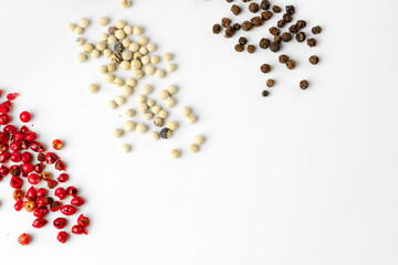 Black, red and white peppercorns scattered on white background