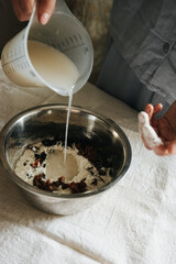woman in blue pajamas prepares homemade bread, adds water to the dough