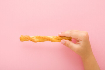 Baby girl hand fingers holding and showing bread stick with cheese on light pink table background. Pastel color. Closeup. Salty snack. Top down view. - obrazy, fototapety, plakaty
