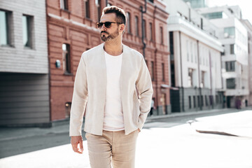 Portrait of handsome confident stylish hipster lambersexual model. Sexy modern man dressed in elegant suit. Fashion male posing in the street background in Europe city at sunset. In sunglasses