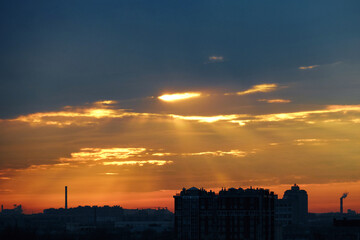 Twilight descends on the city. The rays of the sun shine through the clouds.