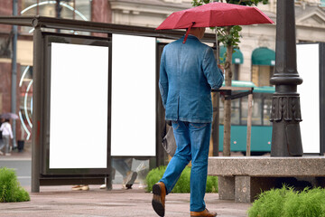 A man in denim clothes walks along the city street under a red umbrella. The male hurries to work...